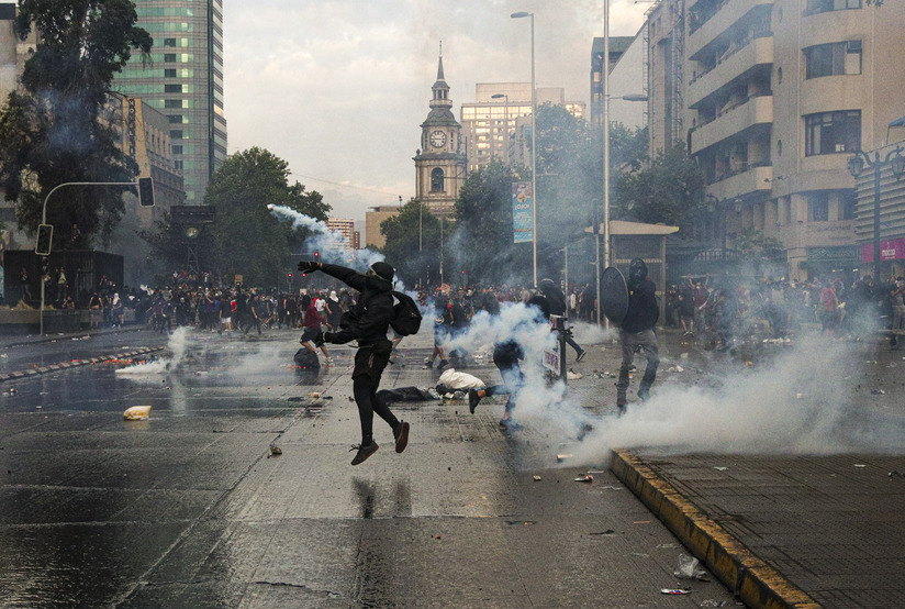 Anarquista arrojando objeto en las calles de Santiago de Chile durante una protesta violenta.